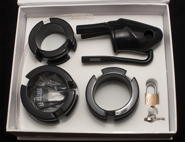 Black HoD100 silicone male chastity device separated into the individual parts including the cage, 3 back rings, a pack of black numbered plastic locks and a brass padlock with 2 keys. All of the parts are sitting in the foam insert inside the supplied storage box.