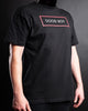 Slave D wearing a black t-shirt with white text inside a red box that says good boy across the chest.