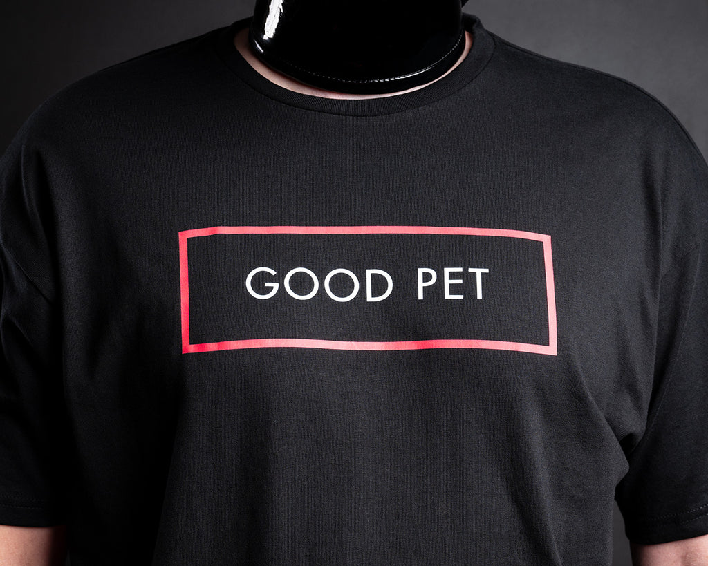 A close-up of a black crewneck t-shirt worn by slave D, featuring a graphic print on the chest with a red rectangular border and the words 'GOOD PET' in white.
