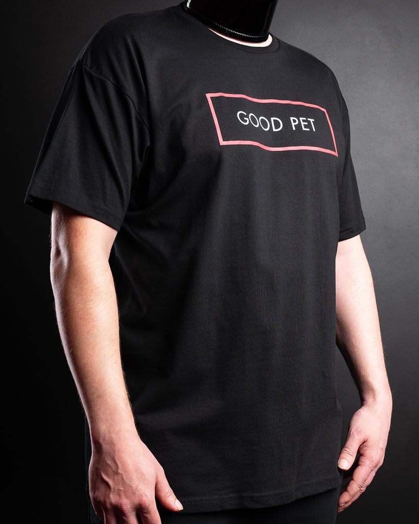 Slave D wearing a black short-sleeve T-shirt with a chest graphic that reads 'GOOD PET' inside a red outlined box, photographed against a dark background.