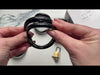Attaching the black cage to one of the four back rings laid out on a marble top table then locking a brass padlock to the kit.